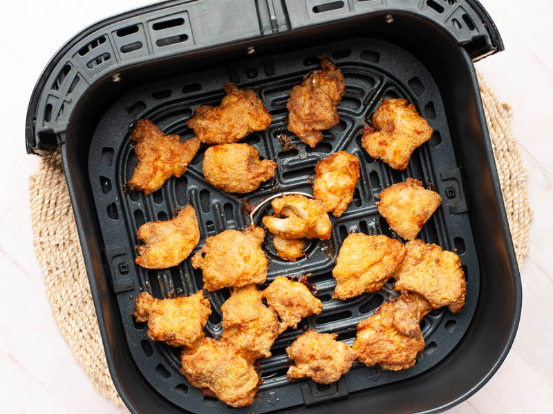Cooked chicken pieces in the basket of an air fryer.