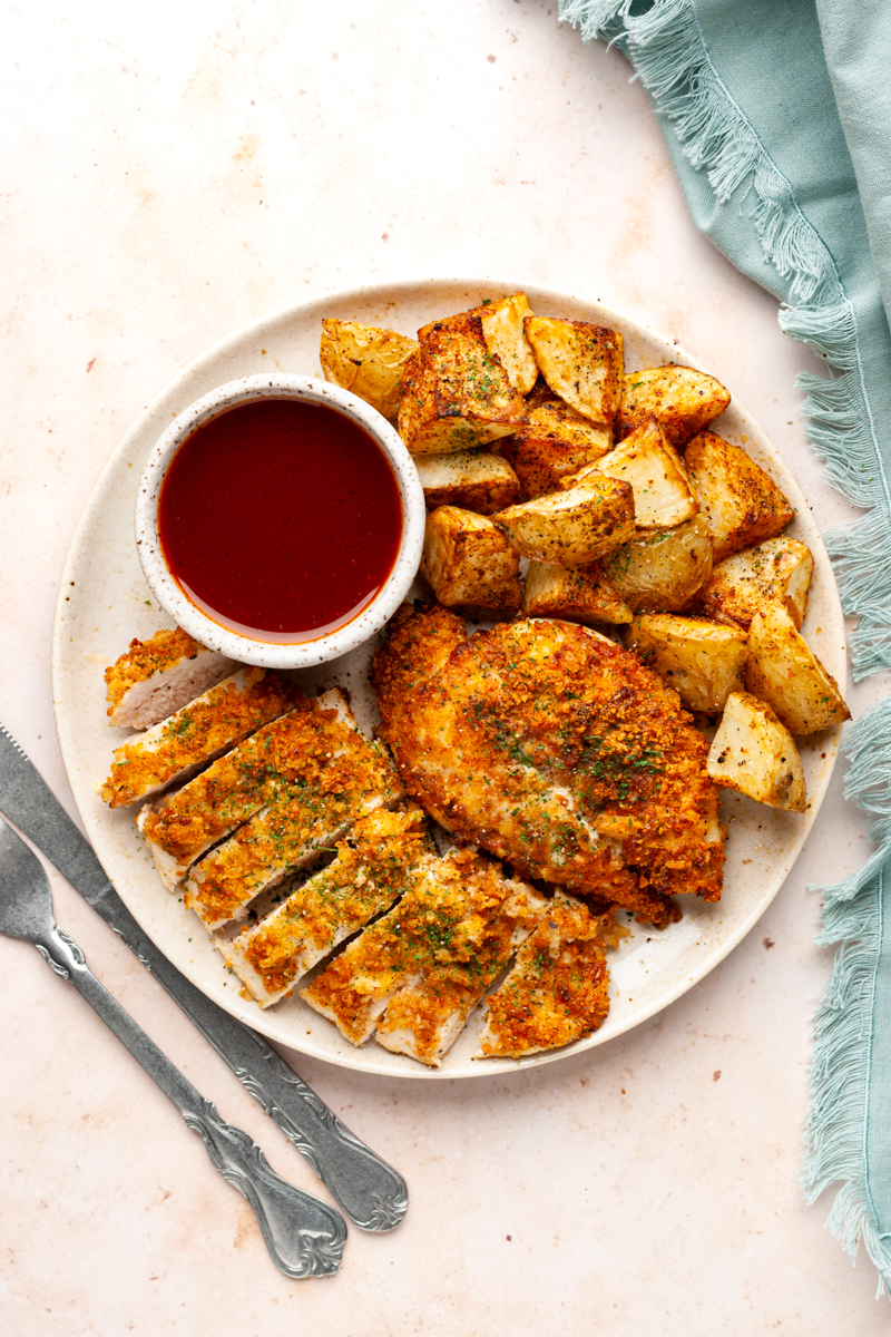 Parmesan crusted chicken breasts, air-fried potato wedges, and sauce on a plate.