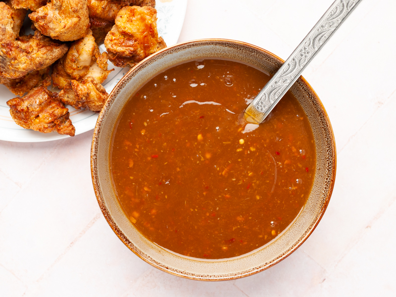 Orange chicken sauce in a bowl with a large spoon. 