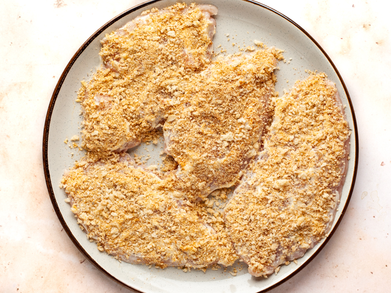 Uncooked parmesan coated halved chicken breasts on plate. 