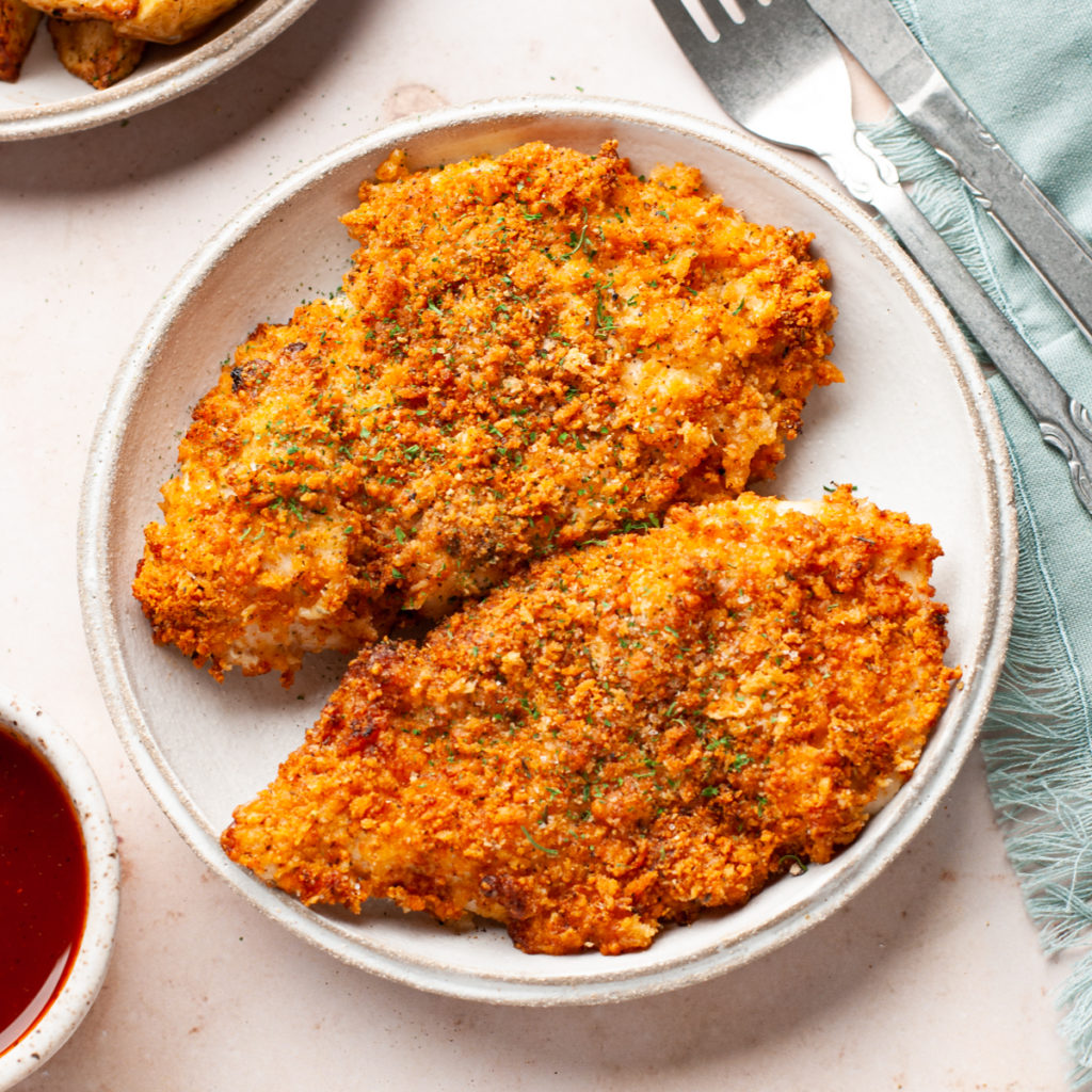 Two parmesan crusted chicken breasts on a plate.