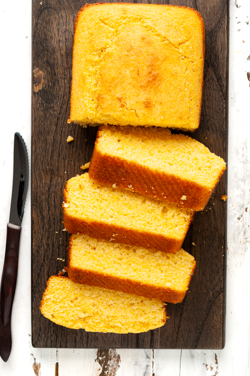Sliced cornbread on a wooden platter with a knife on the side.