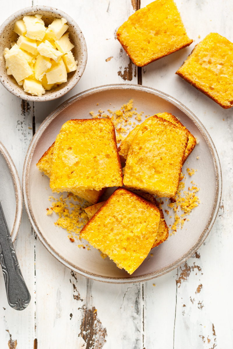 Sliced cornbread on a plate with butter on the side.