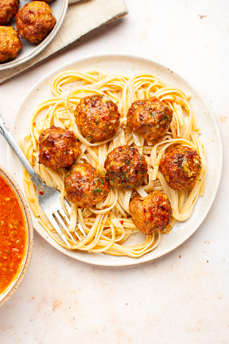chicken meatballs over pasta in a plate with a fork