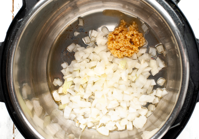 Onions and garlic in oil being sauteed in instant pot. 