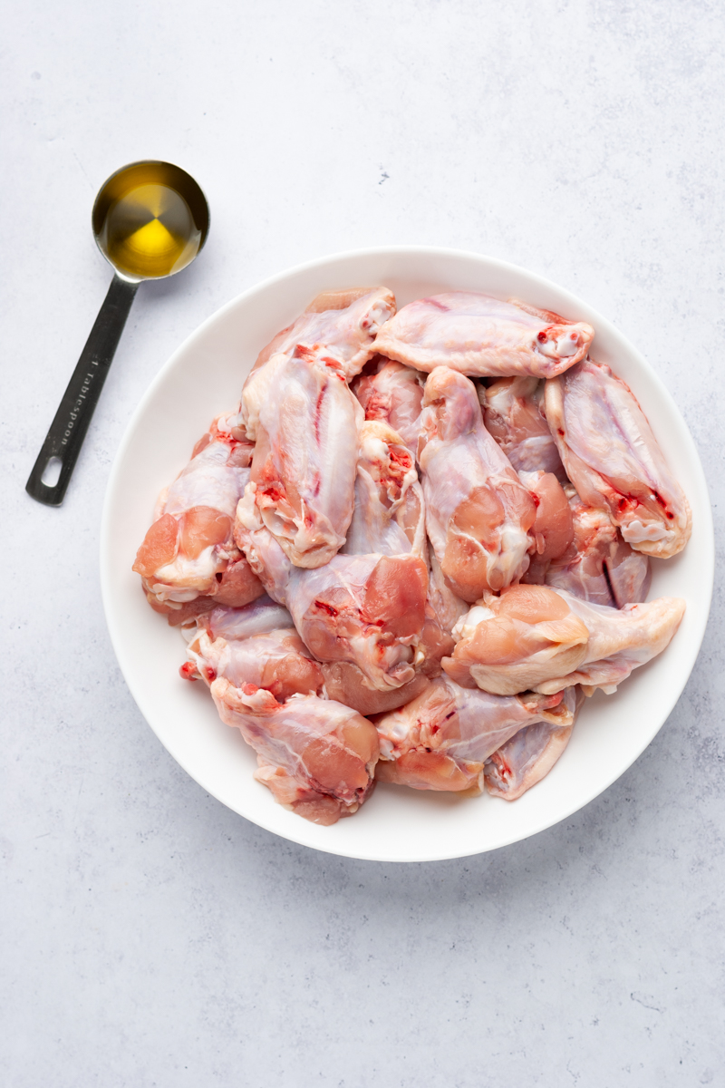 raw chicken wings in a platter and a tablespoon of olive oil