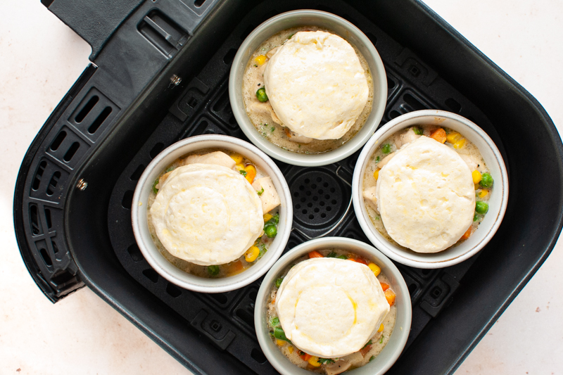 Four ramekins of chicken pot pie topped with uncooked biscuits in an air fryer. 