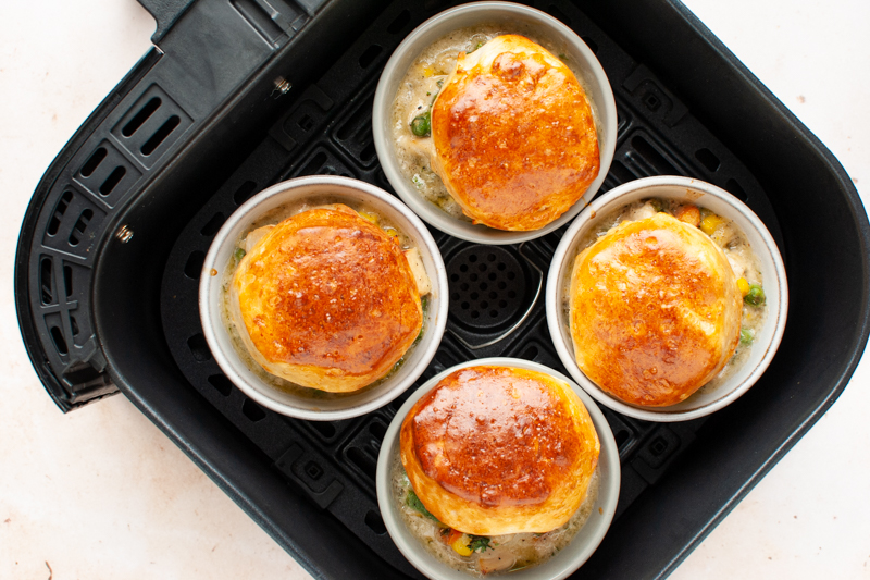 Four chicken pot pies topped with biscuits in an air fryer.