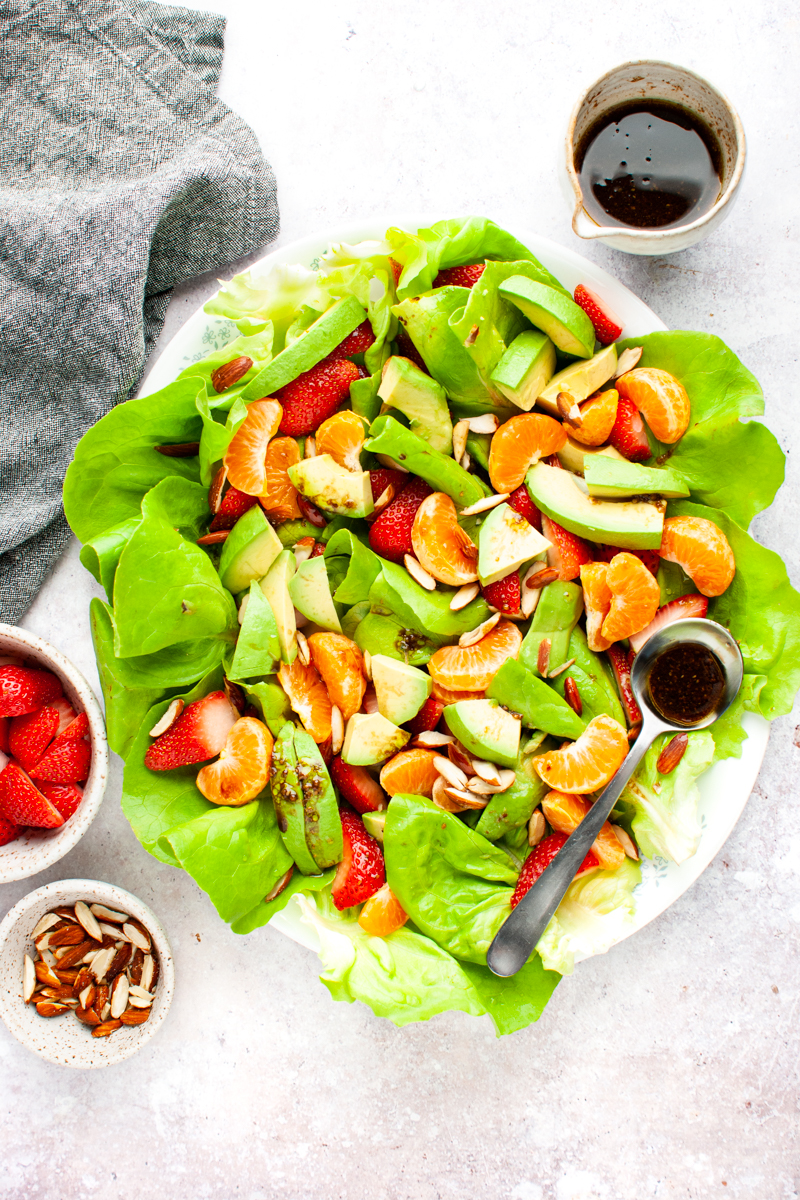 Butter lettuce salad in a platter with a spoon full of balsamic vinegar dressing.