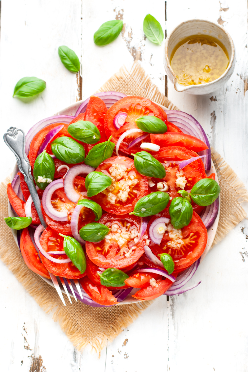 Italian tomato salad on a plate with a fork and dressing in a small jug.