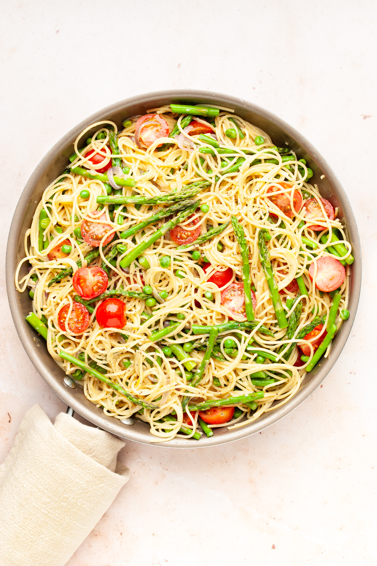 Pasta primavera with asparagus, peas, and cherry tomatoes in a pan.