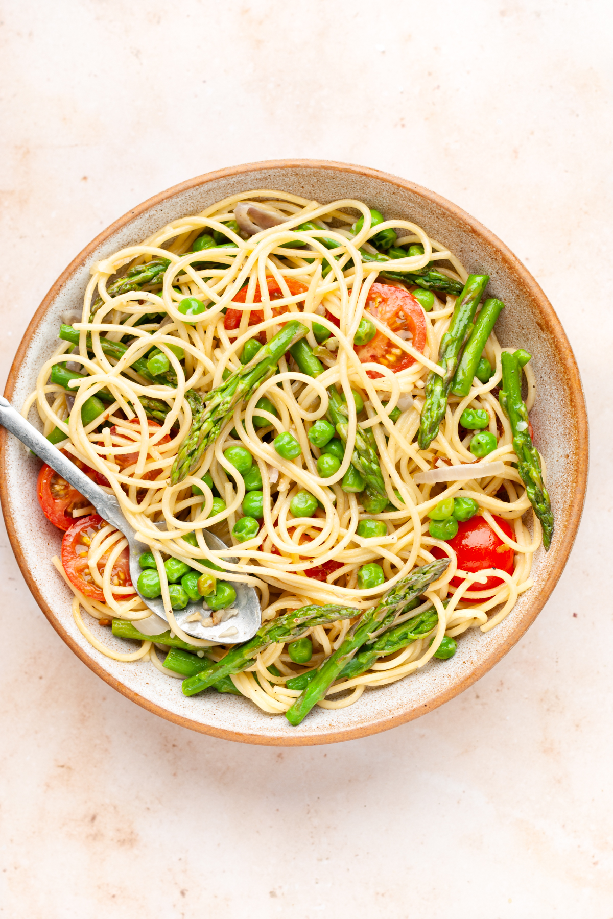 pasta primavera with asparagus, peas, and cherry tomatoes in a bowl with spoon.