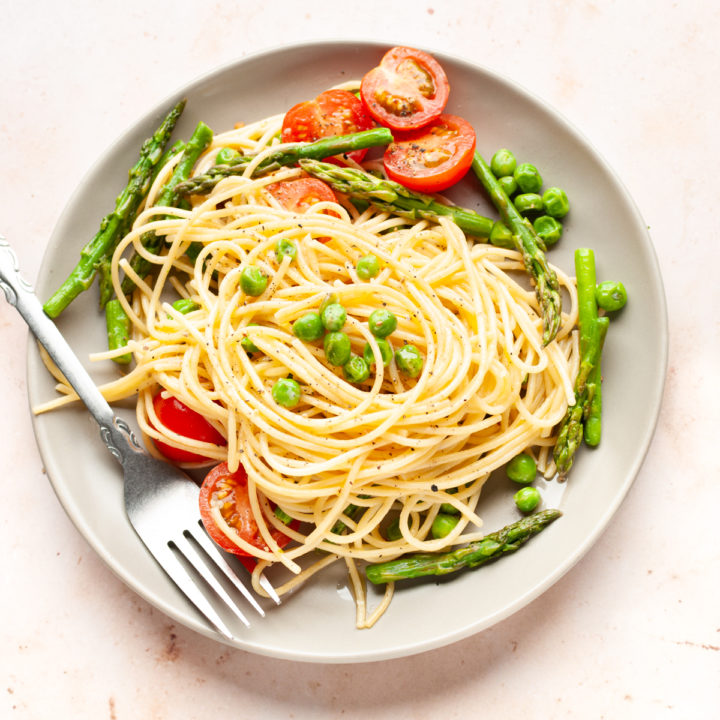 Pasta primavera with asparagus, peas, and cherry tomatoes in a plate with a fork.