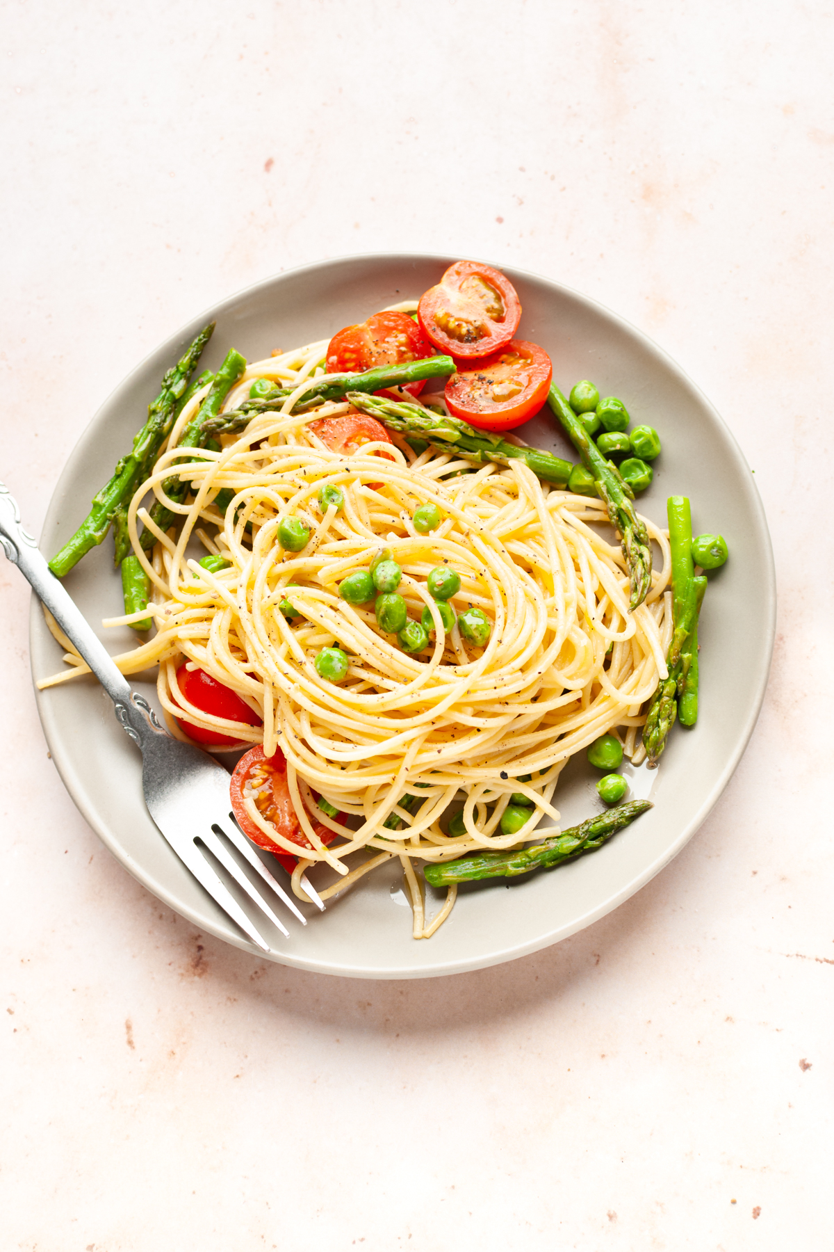 pasta primavera with asparagus, peas, and cherry tomatoes in a plate with fork.