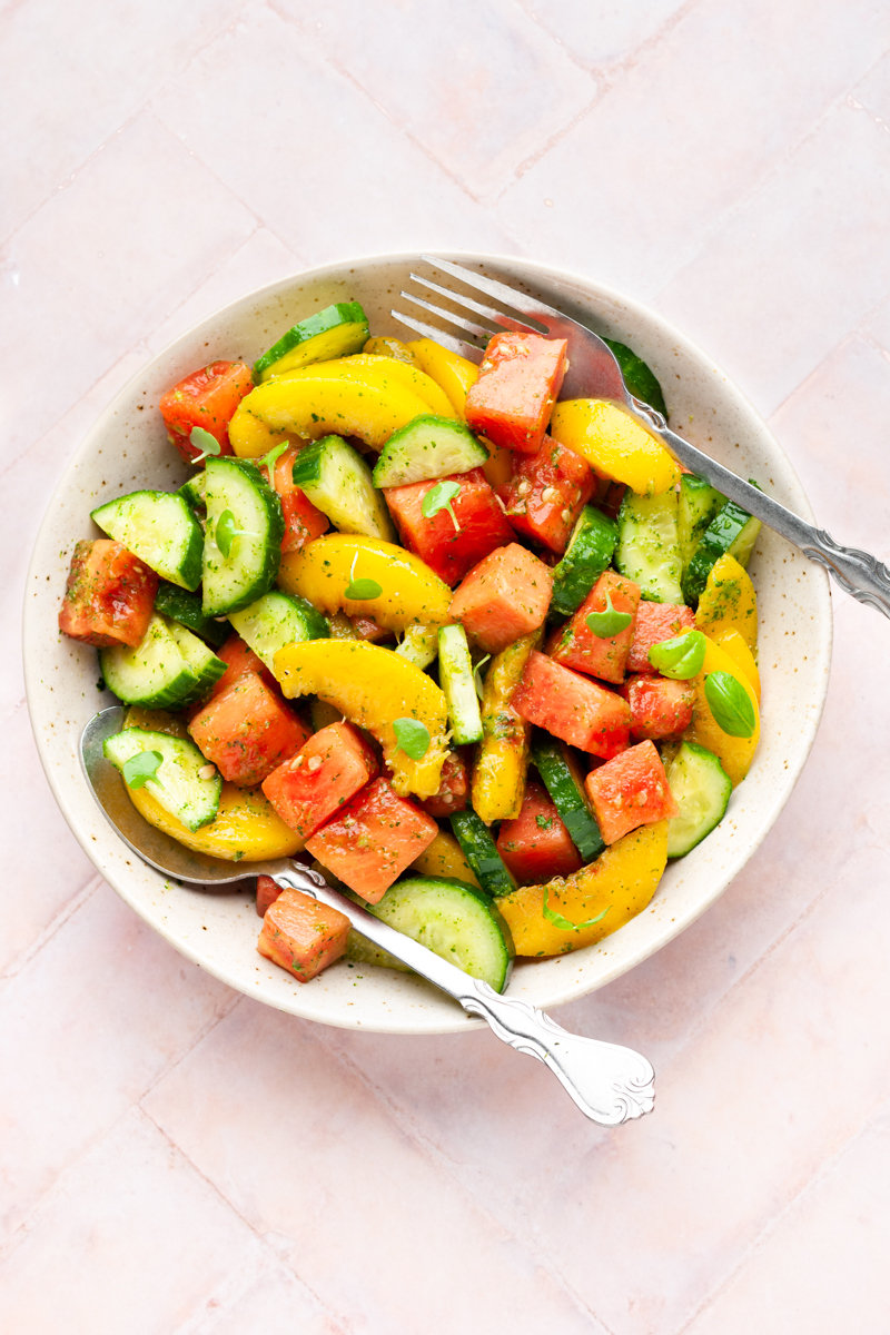 Peach and watermelon salad tossed in sweet basil dressing in a bowl with a fork and spoon. 