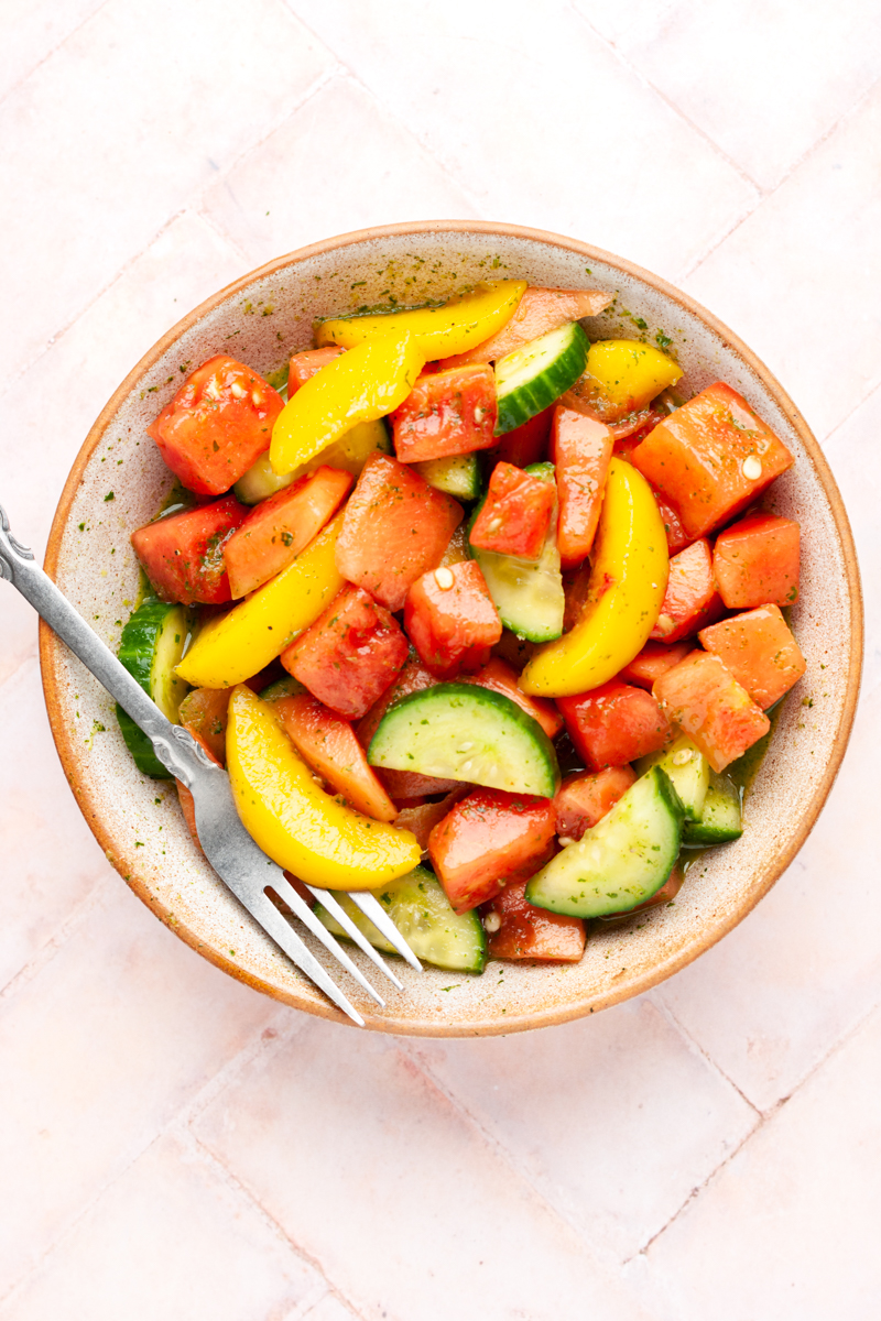 Peach and watermelon salad with cucumbers in a bowl with a fork.