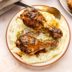 Instant pot chicken drumsticks on a bed of mashed potatoes in a plate.