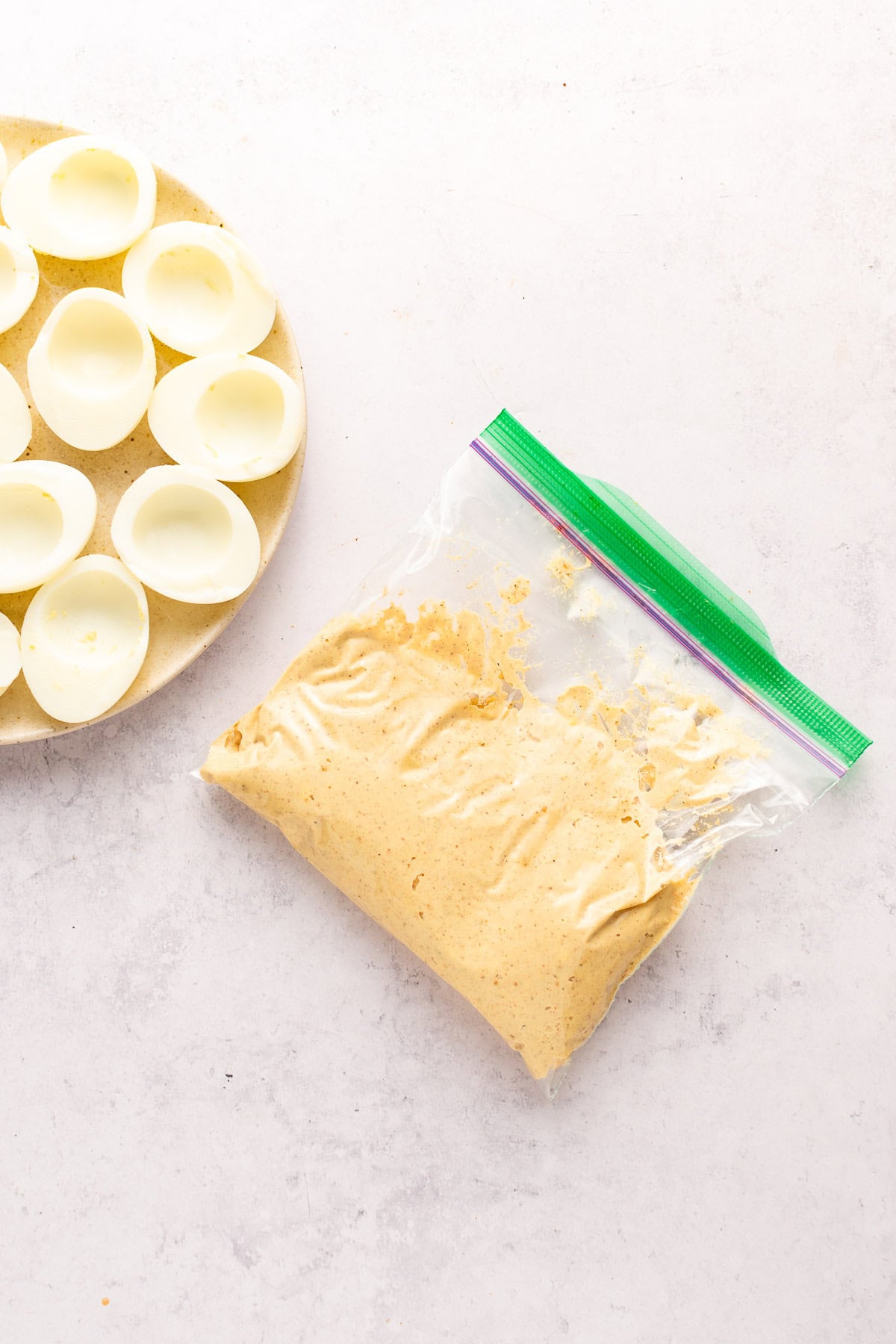 Halved eggs on a plate with the yolks removed and a ziploc bag with filling for the eggs.