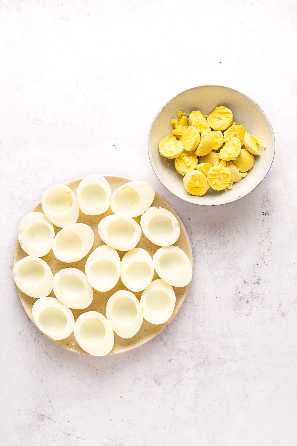 Egg halves with the yolks scooped out; the yolks are in a small bowl next the eggs.