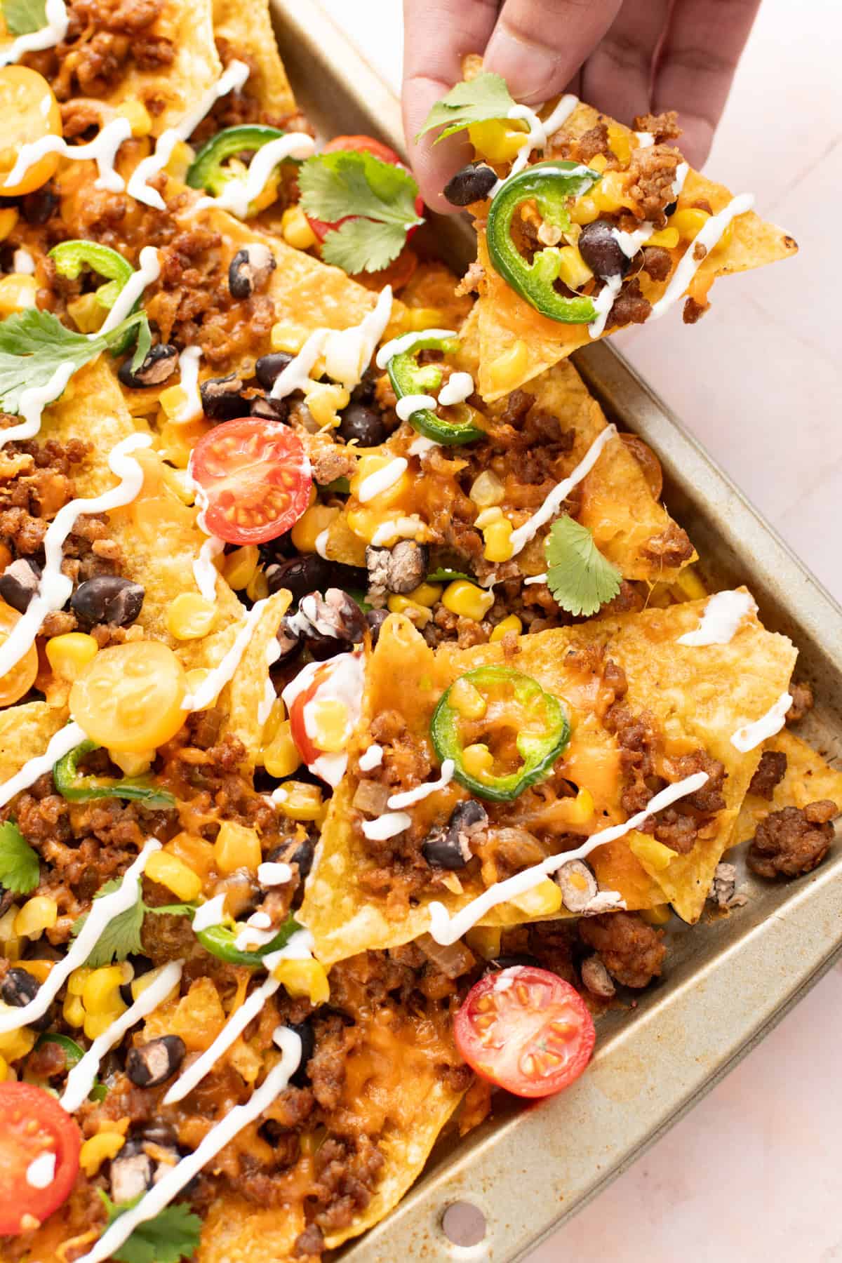 Beef nachos in a sheet pan with a hand over them.