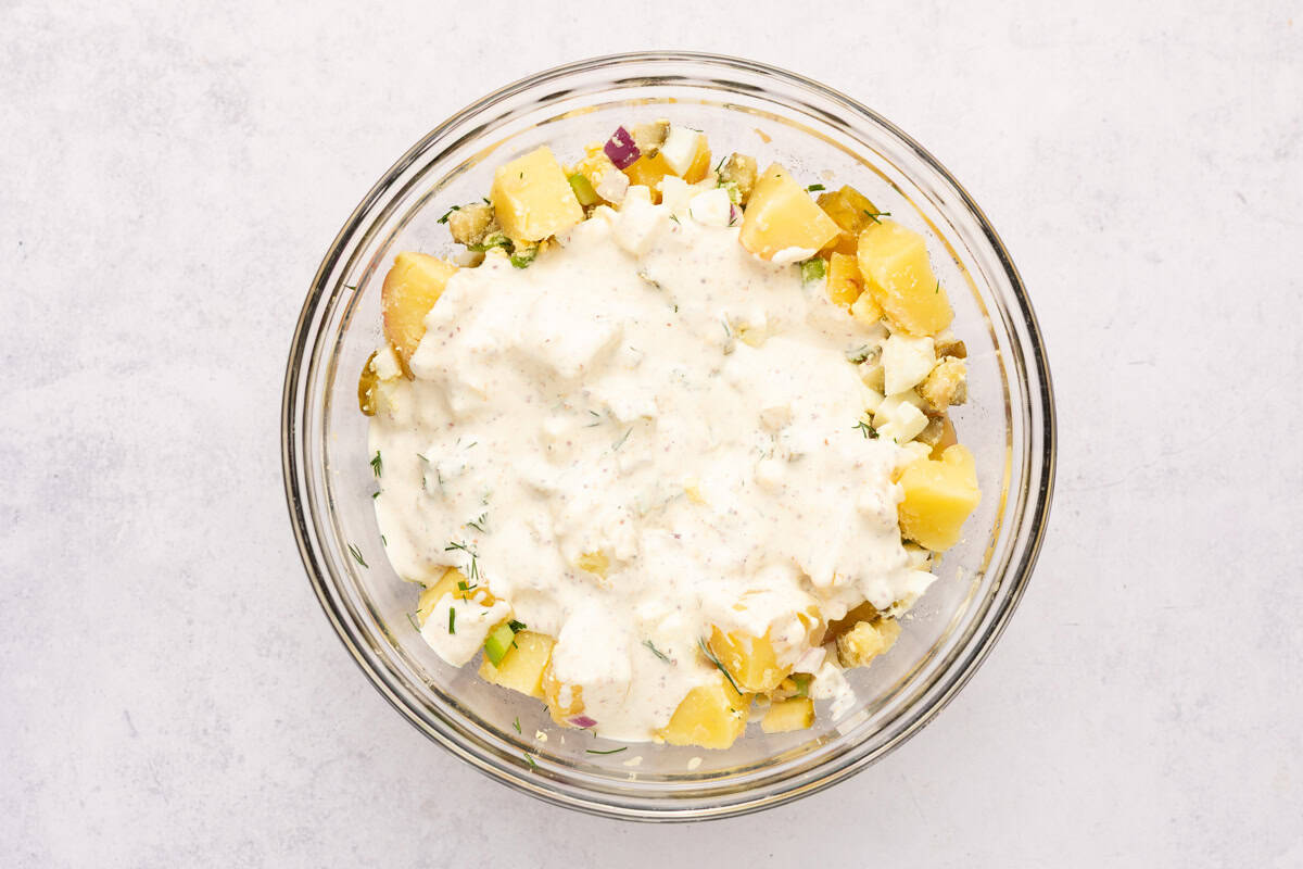 Potato salad ingredients with dressing in a bowl.