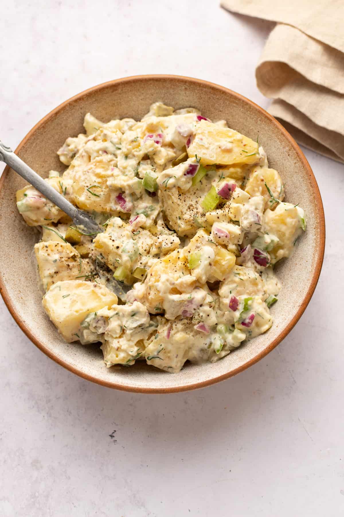 Potato salad with dill pickles in a bowl with a spoon.